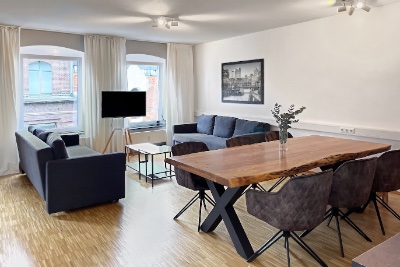 Essbereich mit Massivholztisch und gepolsterten Stühlen, dahinter die weiße Küchenzeile mit Retro-Kühlschrank