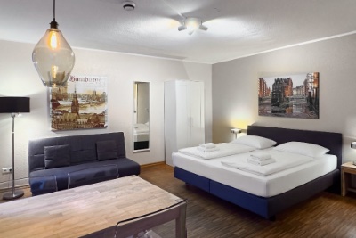 Ferienwohnung Studio: Wohnraum mit Doppelbett, Schlafsofa, Esstisch, weißem Kleiderschrank und Wandbildern