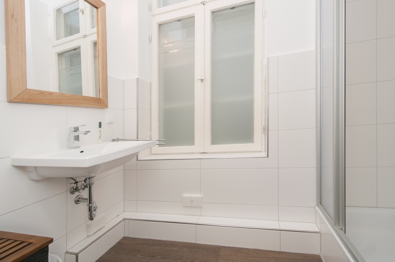 Doppelzimmer Fleetblick: Weiß gefliestes Bad mit Waschbecken, Holzrahmenspiegel, Sprossenfenster mit Milchglas und Duschkabine