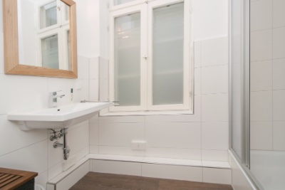 Doppelzimmer Fleetblick: Weiß gefliestes Bad mit Waschbecken, Holzrahmenspiegel, Sprossenfenster mit Milchglas und Duschkabine