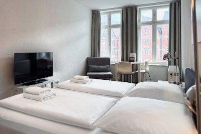 Doppelzimmer Fleetblick: Doppelbett mit Handtüchern, Flachbildfernseher, Sessel und Schreibtisch am Fenster