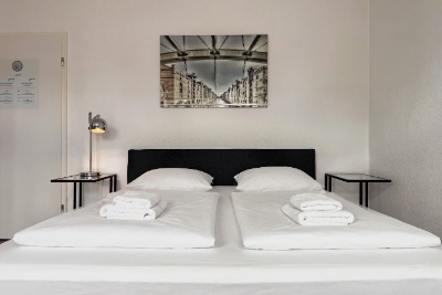 Double room Fleetblick: Double bed with dark headboard, stacked towels, two bedside tables and a table lamp beneath a framed wall picture