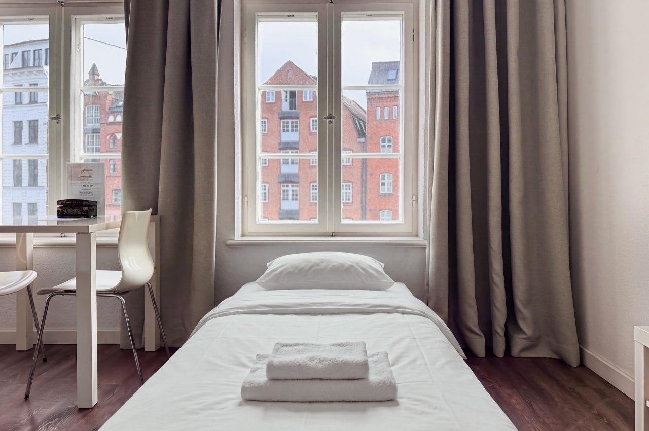 Habitación doble Fleetblick: Cama individual con ropa blanca y toallas dobladas junto a una ventana con cortinas, al lado una mesa con sillas