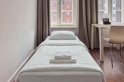 Doppelzimmer Fleetblick: Einzelbett mit weißer Bettwäsche und gestapelten Handtüchern, daneben Schreibtisch mit Stuhl am Fenster