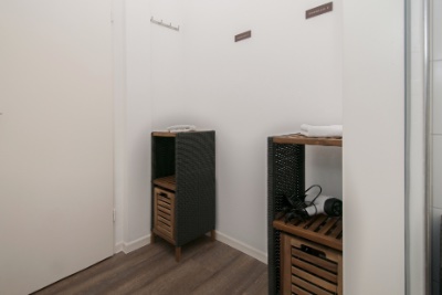 Doppelzimmer Fleetblick: Flurbereich mit zwei Holzregalen mit Handtüchern und Föhn, Wandhaken und Schildern an weißer Wand
