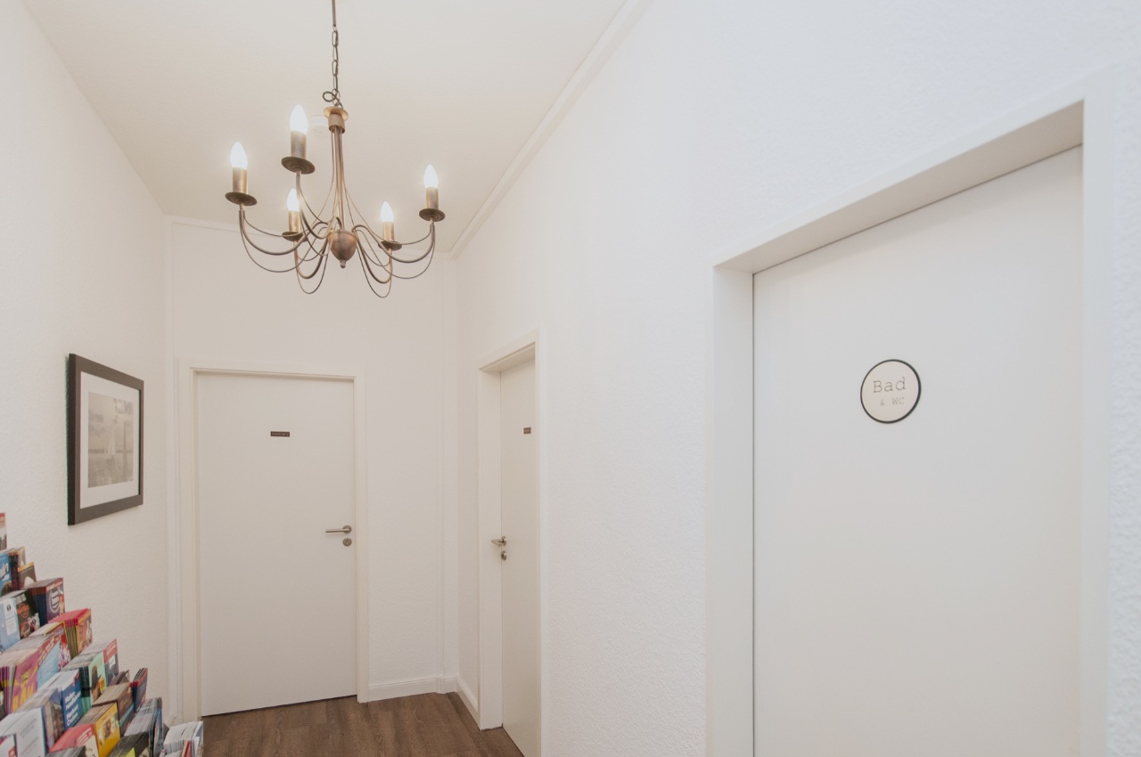 Doppelzimmer Fleetblick: Weißer Flur mit Kronleuchter, mehreren Türen, Türschild und Prospektständer