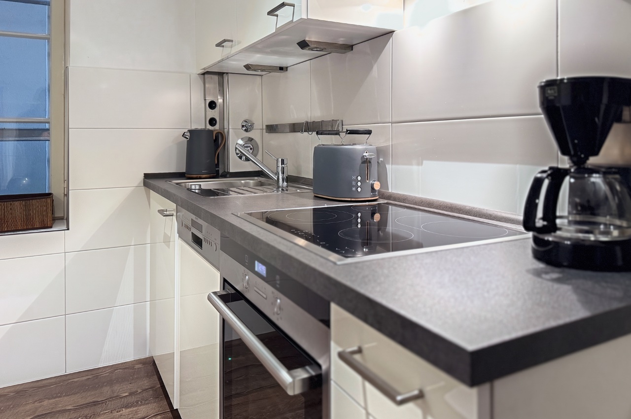 Habitación doble Fleetblick: Cocina blanca con encimera oscura, placa vitrocerámica, horno, fregadero, tostadora y cafetera