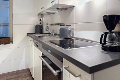 Habitación doble Fleetblick: Cocina blanca con encimera oscura, placa vitrocerámica, horno, fregadero, tostadora y cafetera