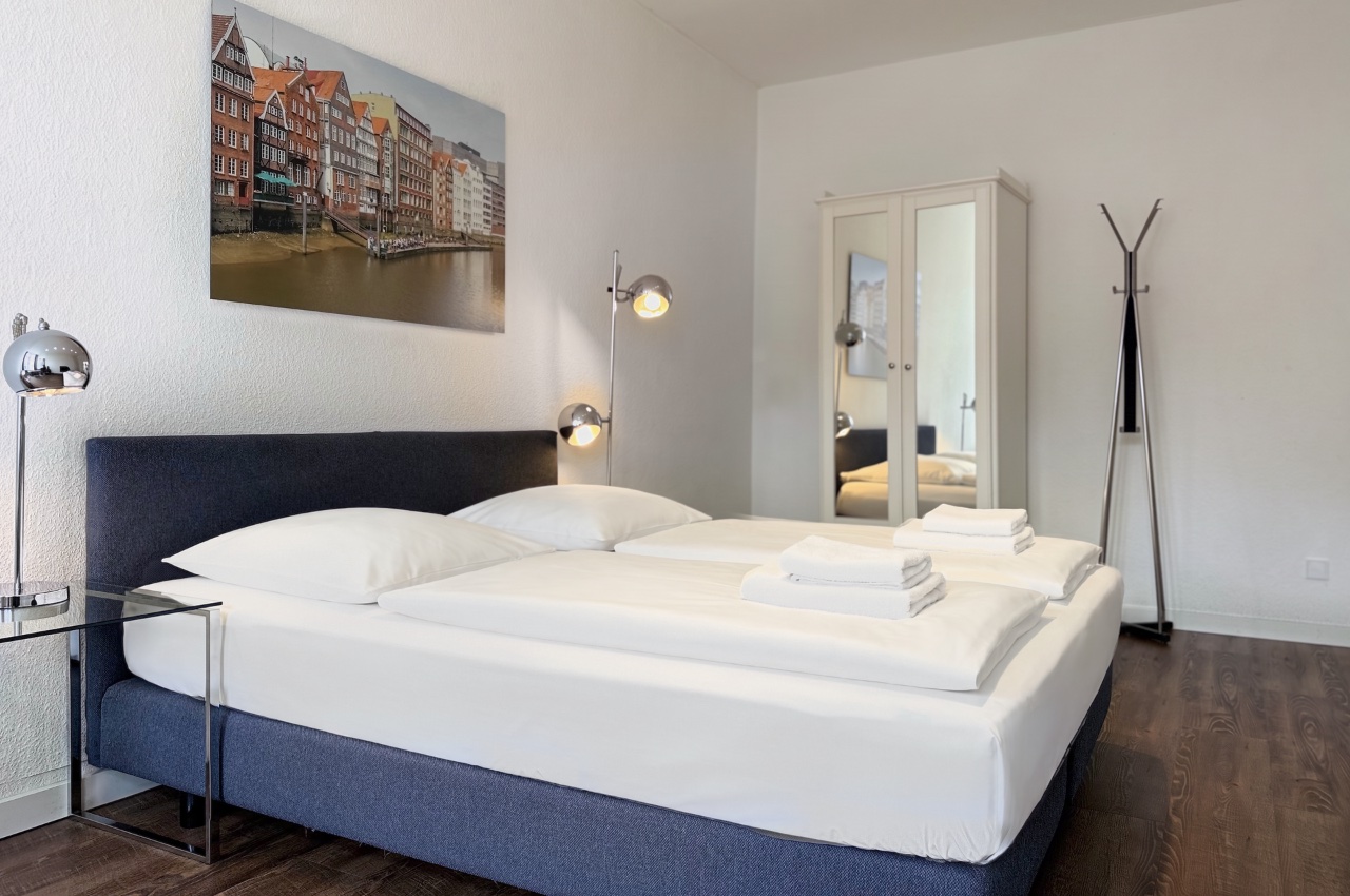 Doppelzimmer Fleetblick: Doppelbett mit Polsterkopfteil, Handtüchern, Wandbild, Spiegelschrank und Garderobenständer