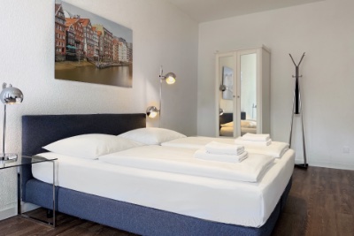 Doppelzimmer Fleetblick: Doppelbett mit Polsterkopfteil, Handtüchern, Wandbild, Spiegelschrank und Garderobenständer
