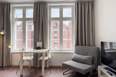 Habitación doble Fleetblick: Zona de estar con mesa blanca, dos sillas, sillón gris, televisor y dos ventanas con cortinas